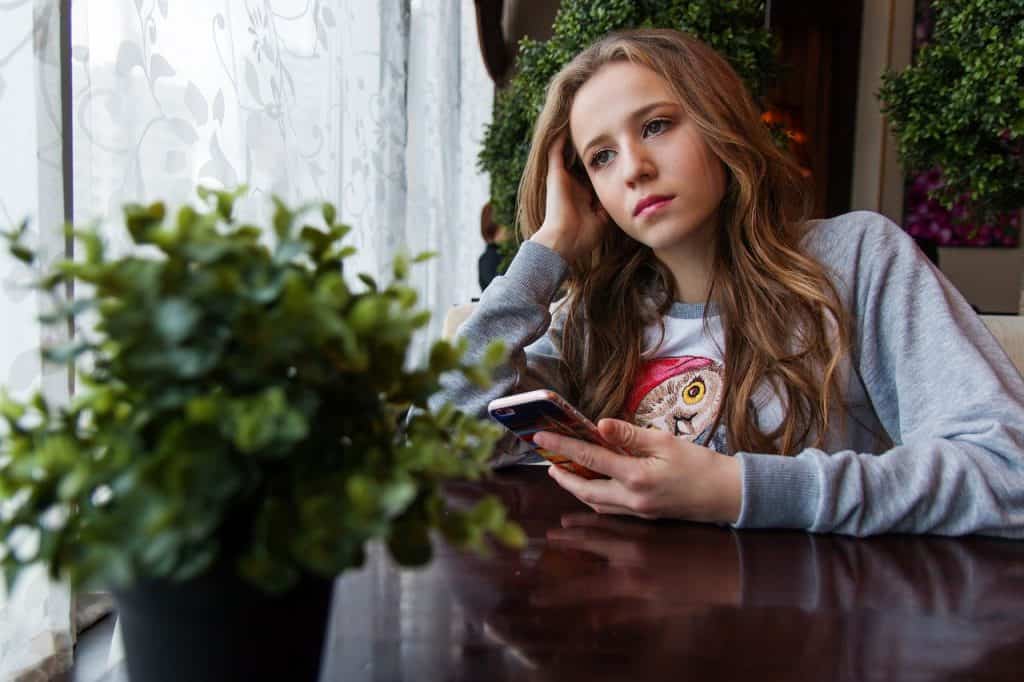 Meisje met smartphone voor haar uit aan het staren in huis